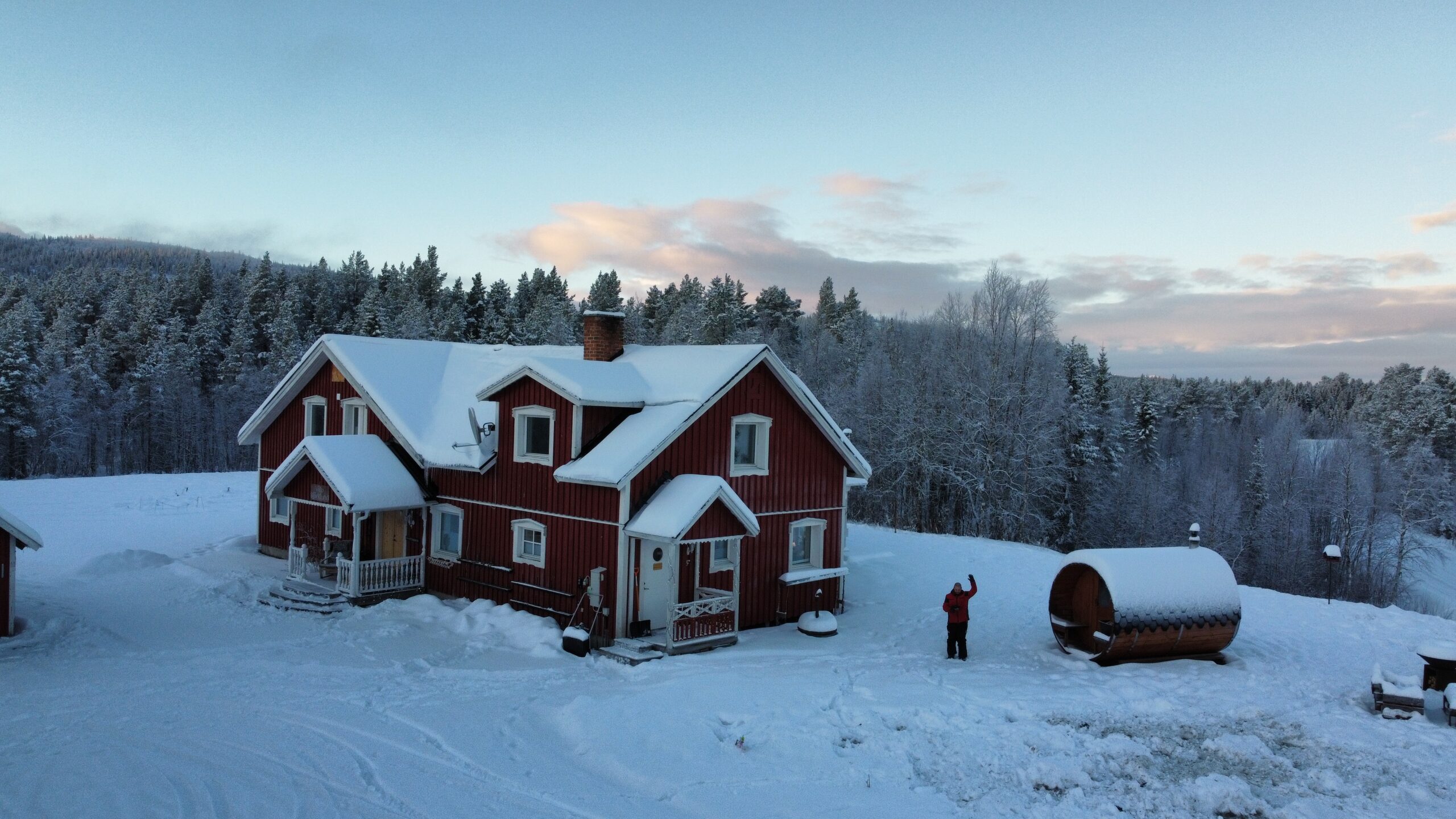 Röd trästuga i snön med skog i bakgrunden