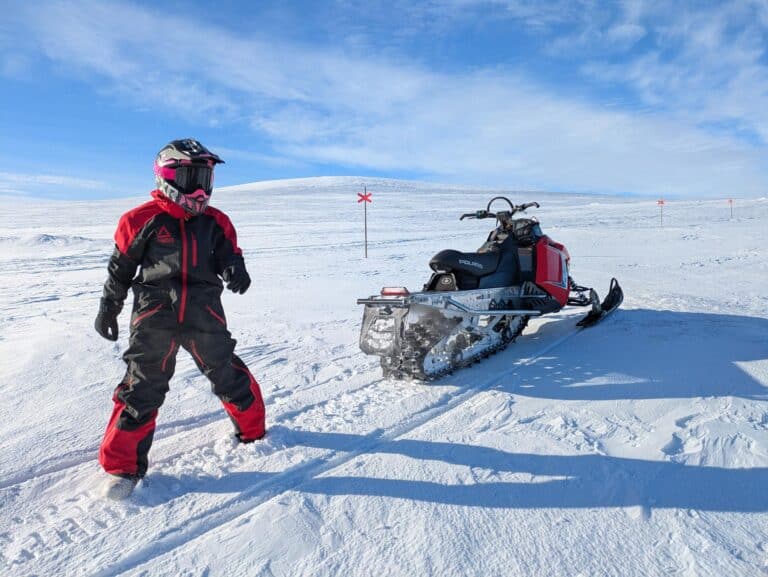 Person in warmer Kleidung neben einem Schneemobil.