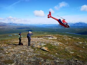 Personen beobachten einen fliegenden Hubschrauber in der Landschaft