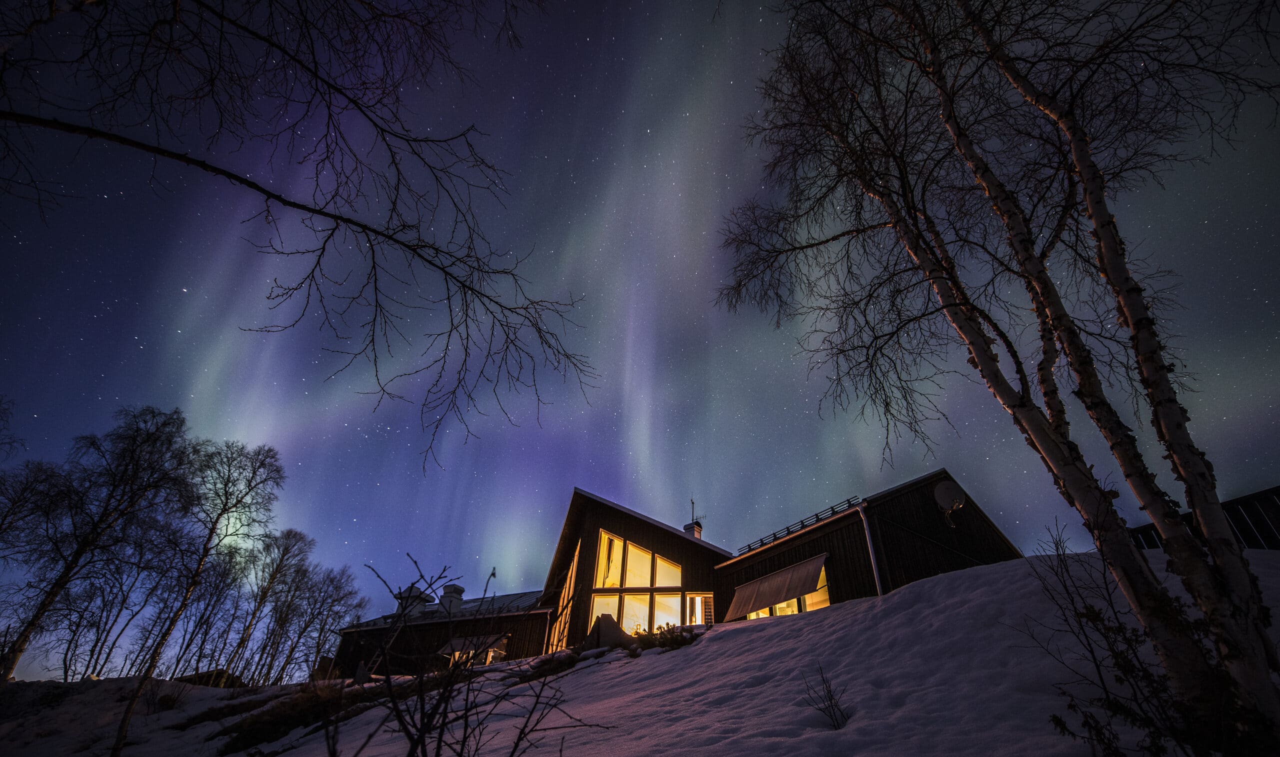 Polarlichter über beleuchtetem Haus im Schnee