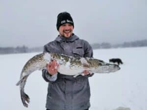 Mann hält großen Fisch im Schnee.