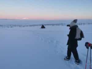Person im Schnee mit Schneemobil im Hintergrund