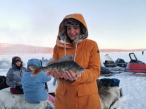 Frau in orangeem Anorak hält einen Fisch.