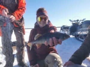 Frau hält frisch gefangenen Fisch im Schnee.