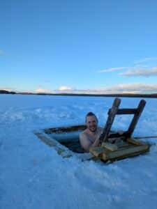 Mann lächelt aus einem Eisloch im Schnee.