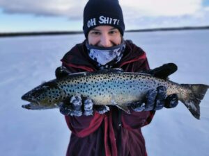 Person hält einen gefangenen Fisch im Schnee.