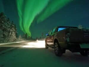 Nordlichter über einer verschneiten Straße und Auto