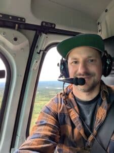 Mann im Hubschrauber mit Kopfhörern und Landschaft.