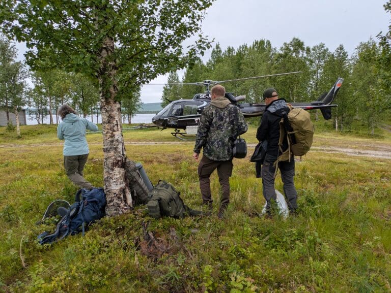Drei Personen stehen vor einem Hubschrauber in der Natur.